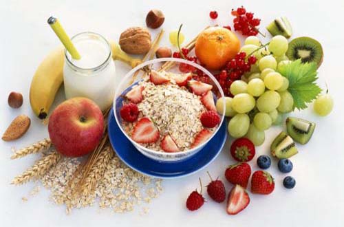 Bowl of muesli, surrounded with fruit, nuts and cereals